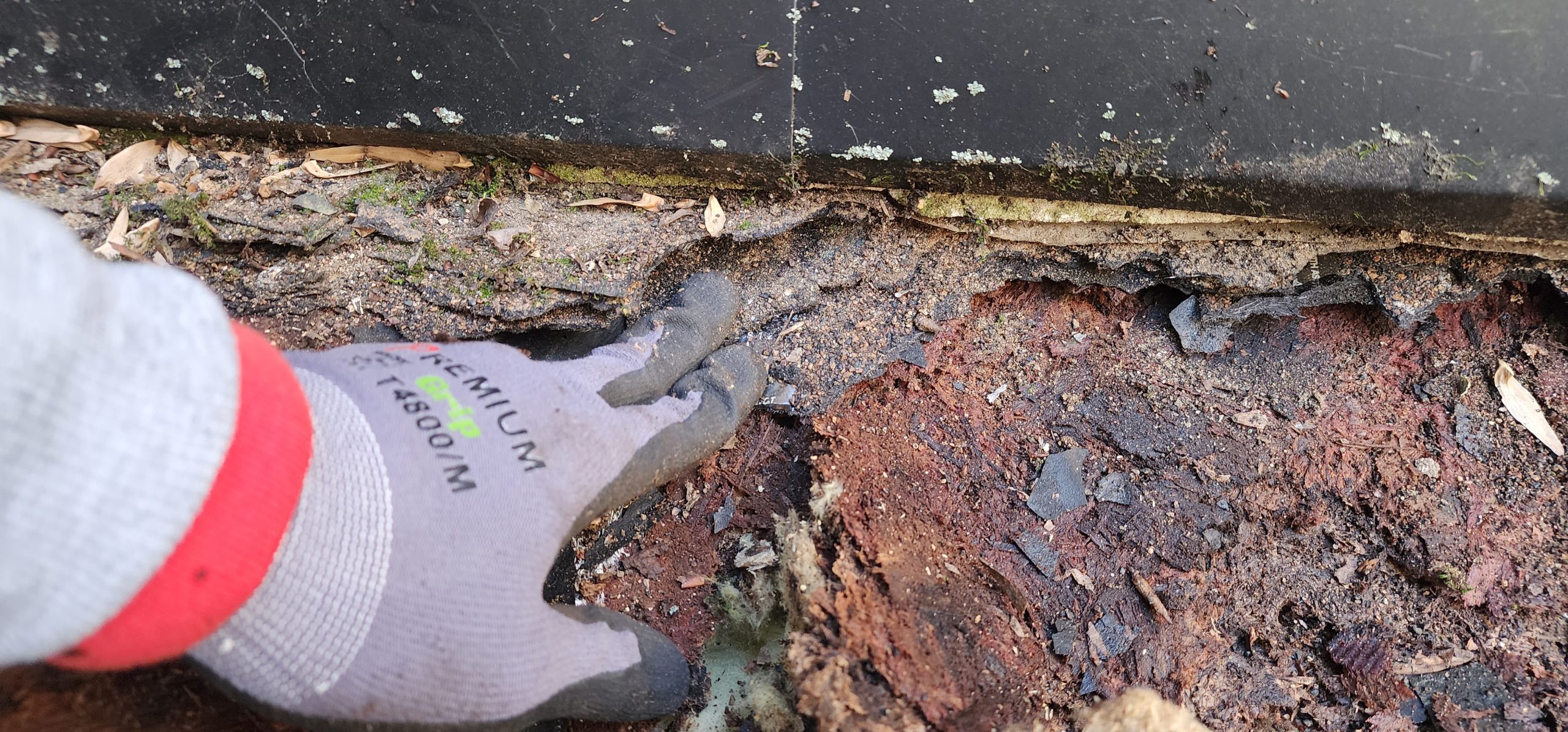 Close-up of deteriorated roofing material being inspected by hand during a repair assessment