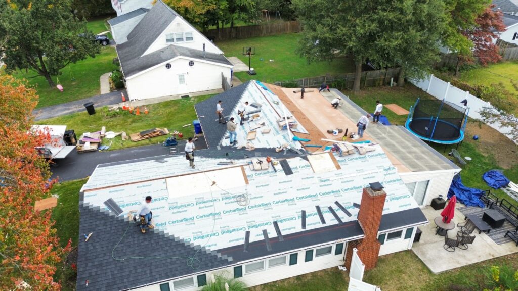 Aerial view of a roof replacement in progress, with underlayment laid across the house and the crew working along the ridge