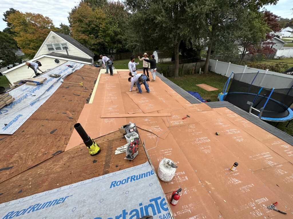Crew rolling out synthetic underlayment across a prepared roof deck during a replacement