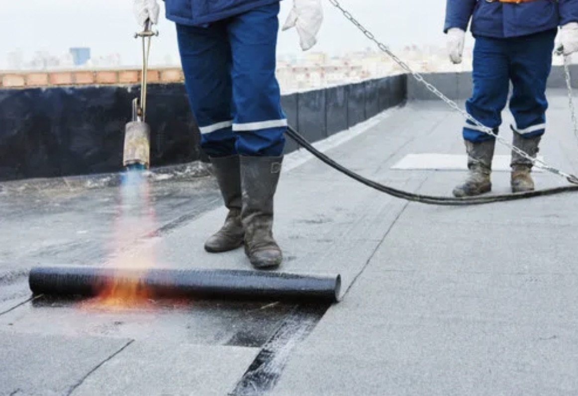 Roofing crew applying a torch-down modified bitumen membrane on a flat commercial roof