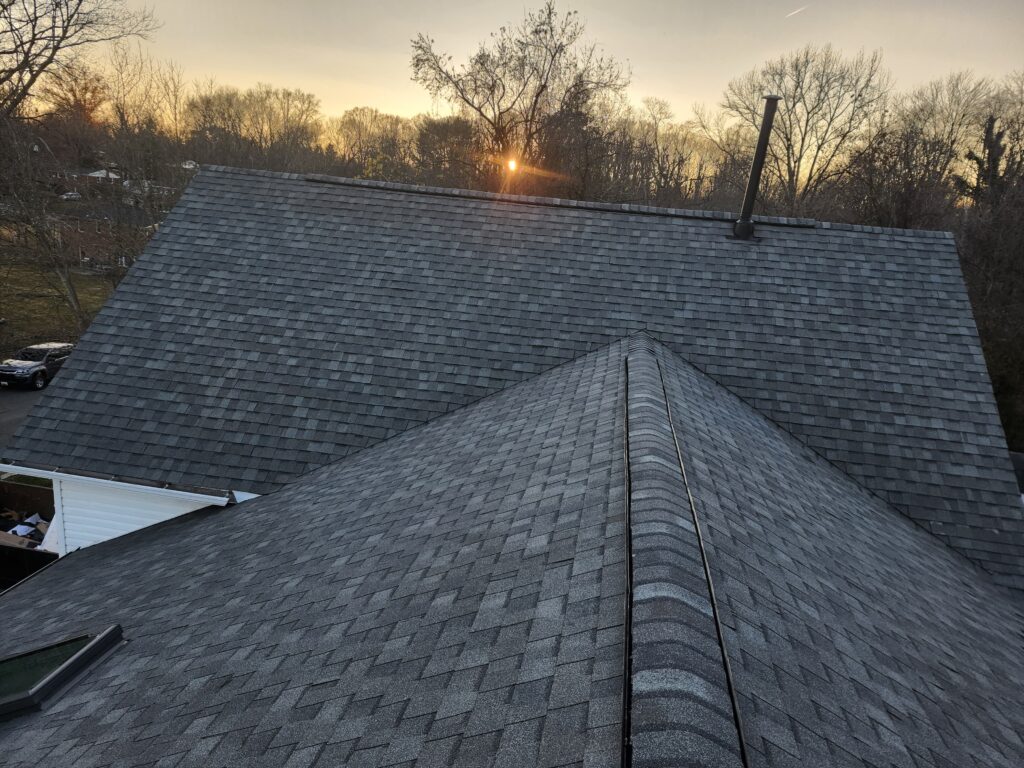 Completed shingle roof photographed at sunset, the ridge line running out toward the treeline