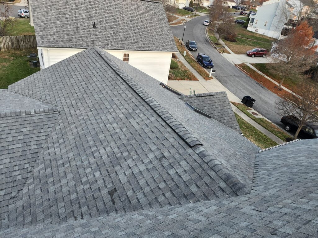 Finished architectural shingle roof photographed from above, ridge and hips complete, with the street and neighbouring homes beyond