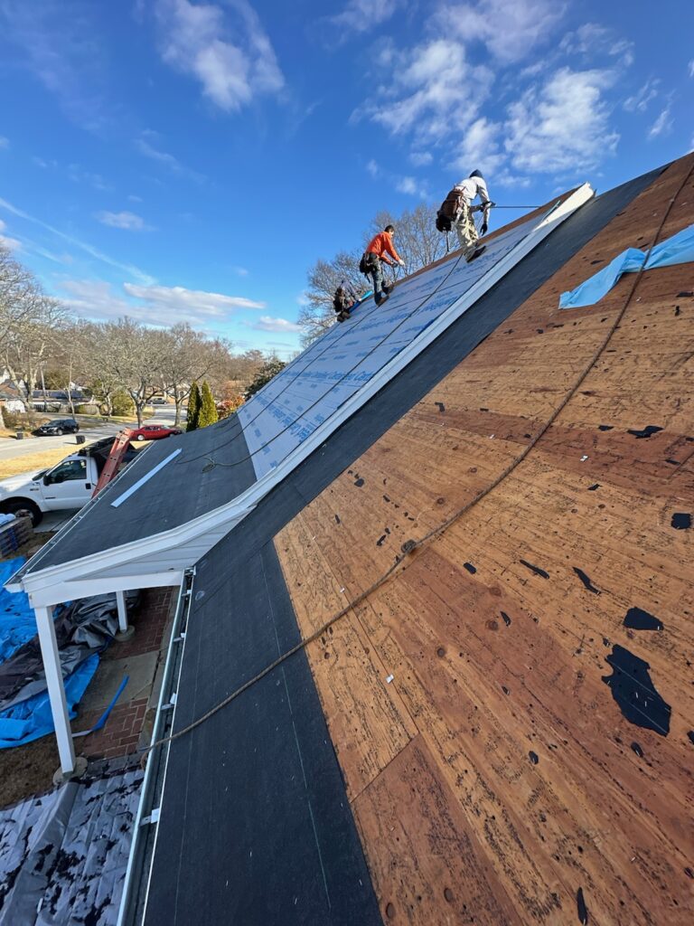 Crew working along a steep roof plane against a clear blue sky during a replacement