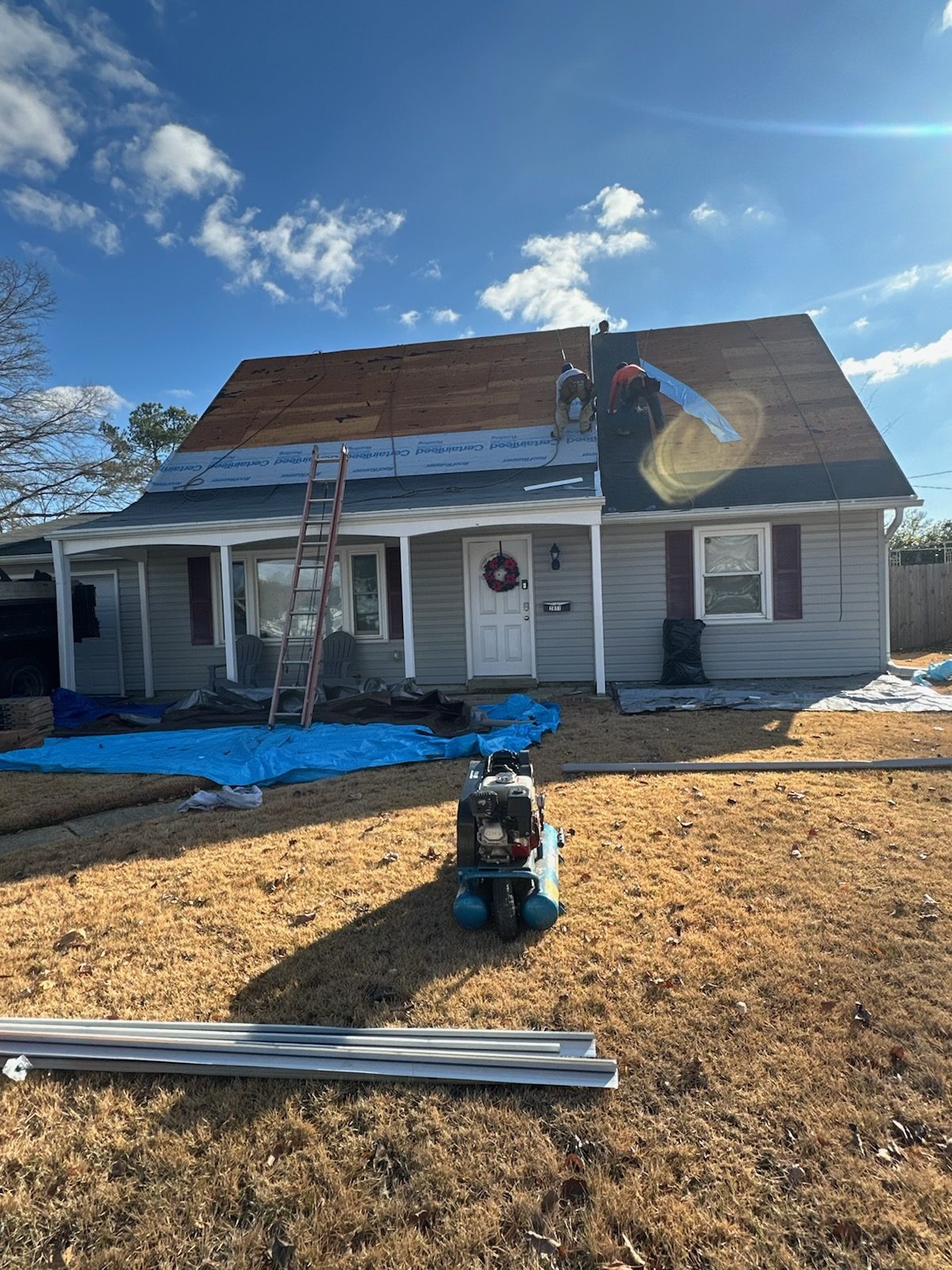 Hernandez Roofing Pros crew mid-installation on a home's roof, with landscaping protected below