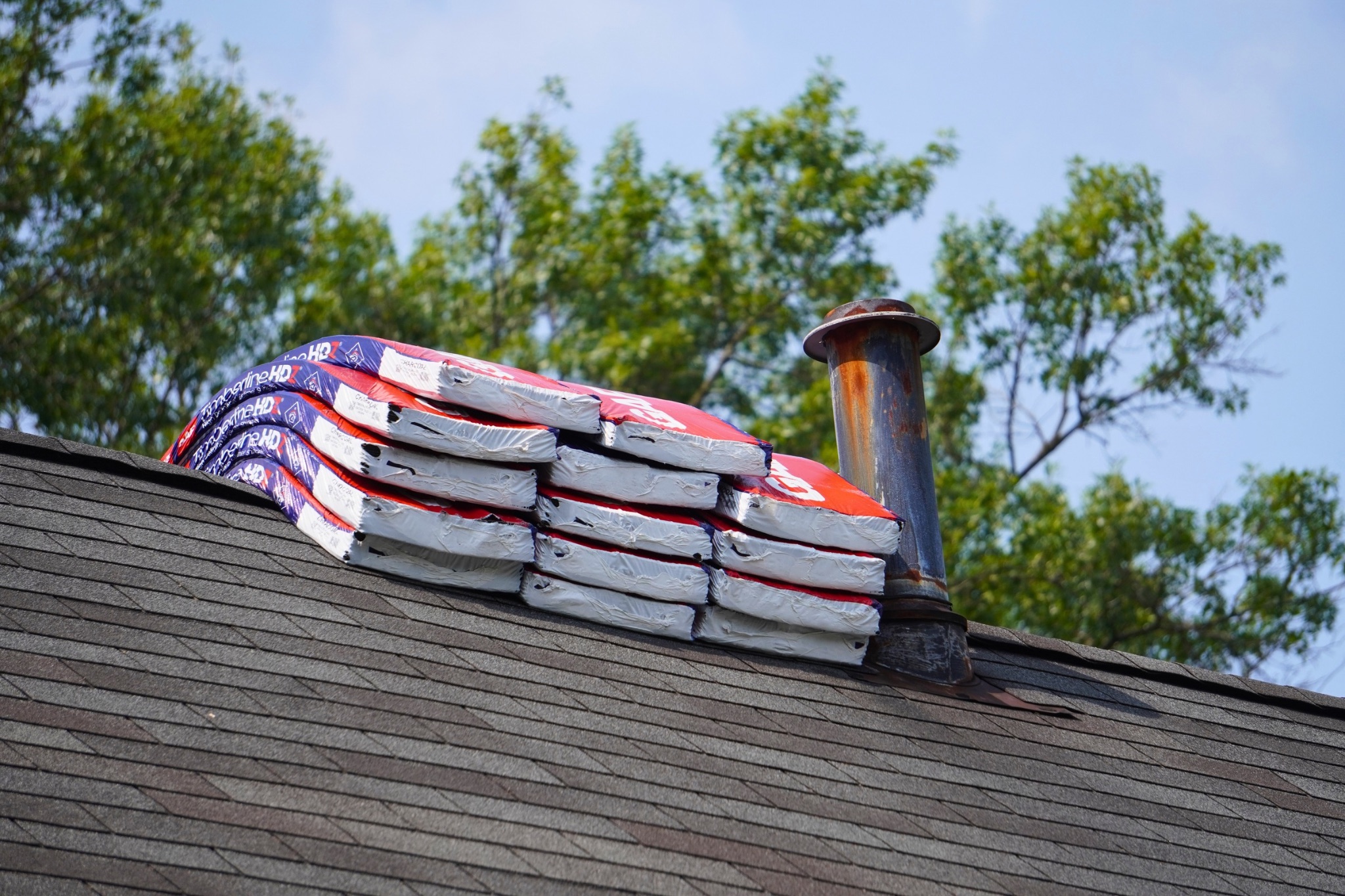 Bundles of architectural shingles staged along a roof ridge beside a vent pipe before installation
