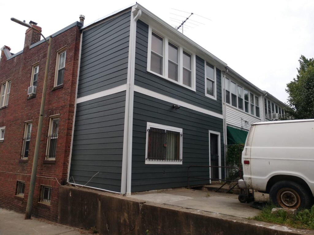 The same rear addition after new dark gray siding installation, with matching white trim