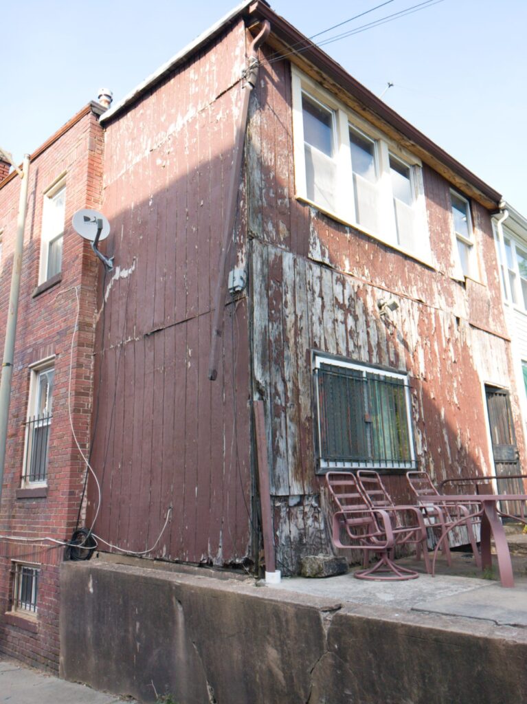 Severely weathered wood-plank siding with peeling paint on a rowhouse rear addition