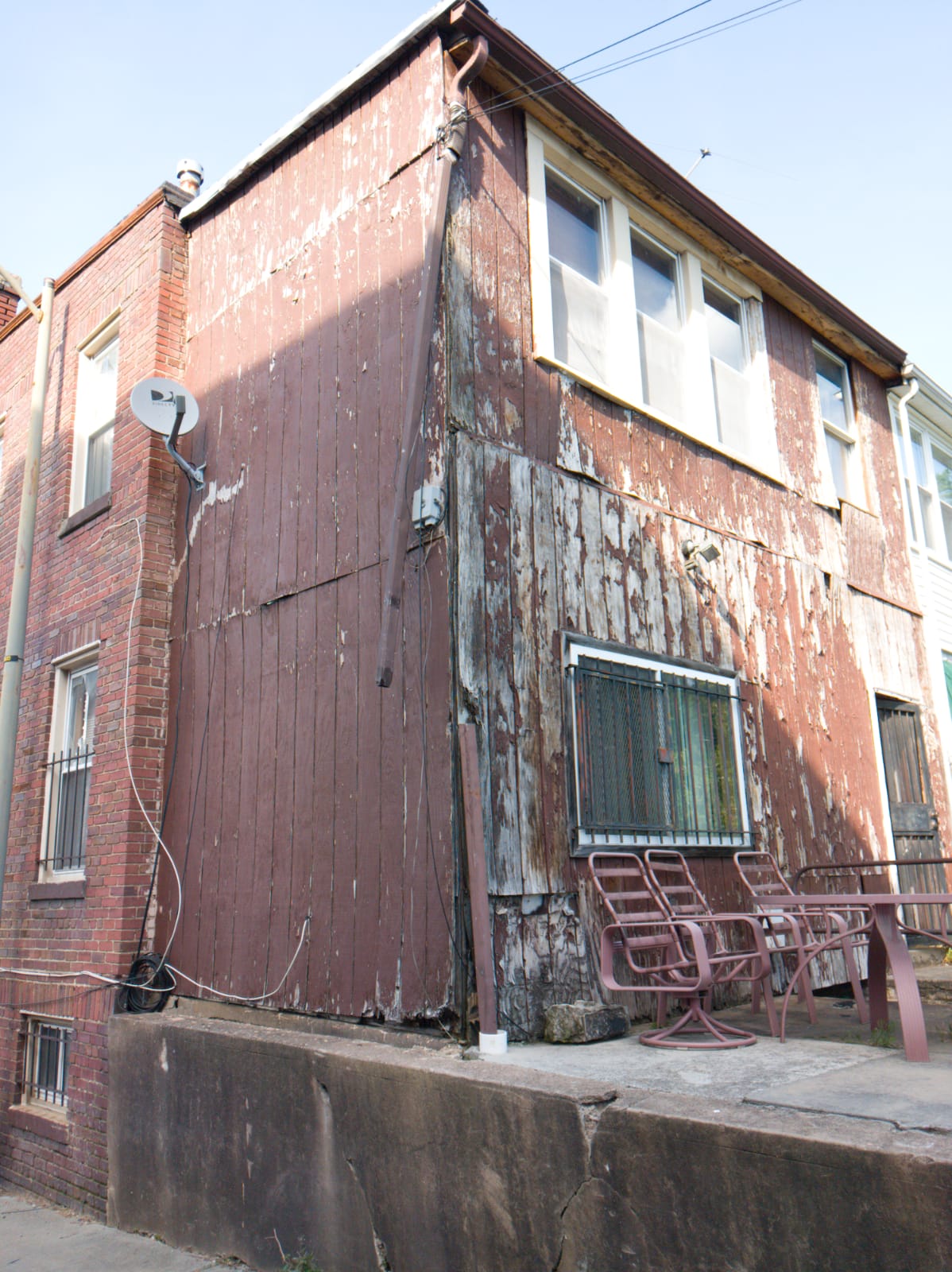 Severely weathered wood-plank siding with peeling paint on a rowhouse rear addition