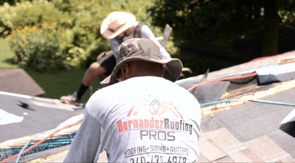 Hernandez Roofing Pros crew member in a branded company shirt working on a roof tear-off