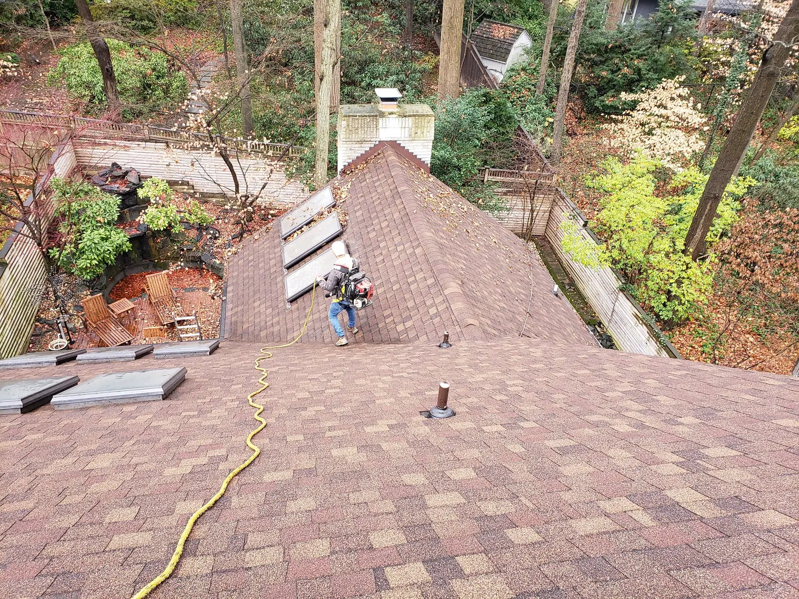 Elevated view across a large shingled roof with wooded grounds below during a roof inspection