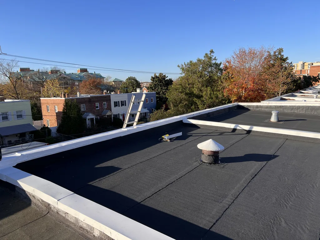 Completed torch-down flat roof with a new white parapet cap under a clear blue sky in Alexandria, Virginia