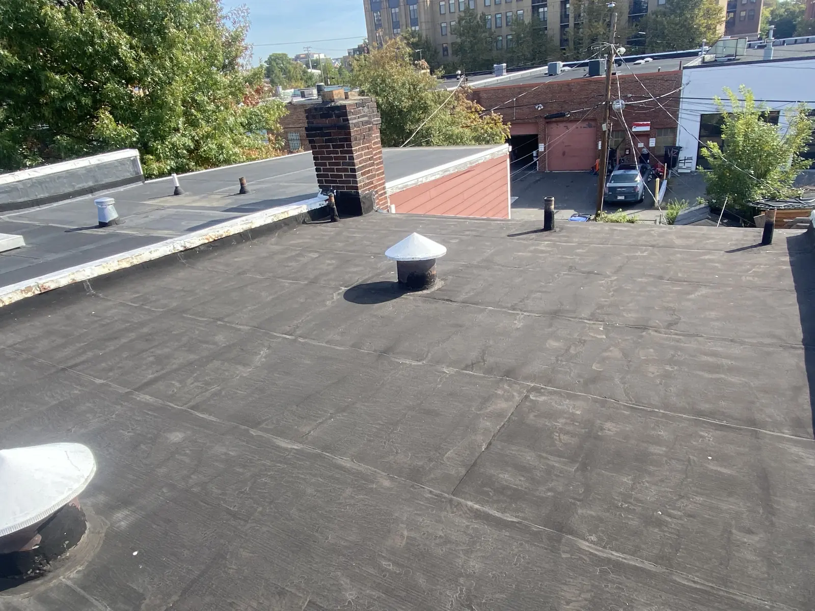 Existing flat roof with a brick chimney and mature trees before replacement in Alexandria, Virginia