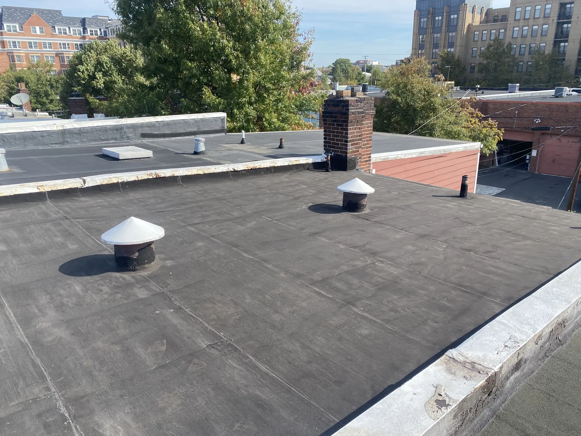 Worn low-slope flat roof with vent stacks and a brick chimney before a torch-down replacement in Alexandria, Virginia