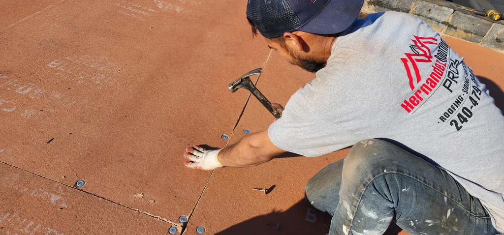 Hernandez Roofing Pros crew member in a branded shirt kneeling to finish a new roof surface