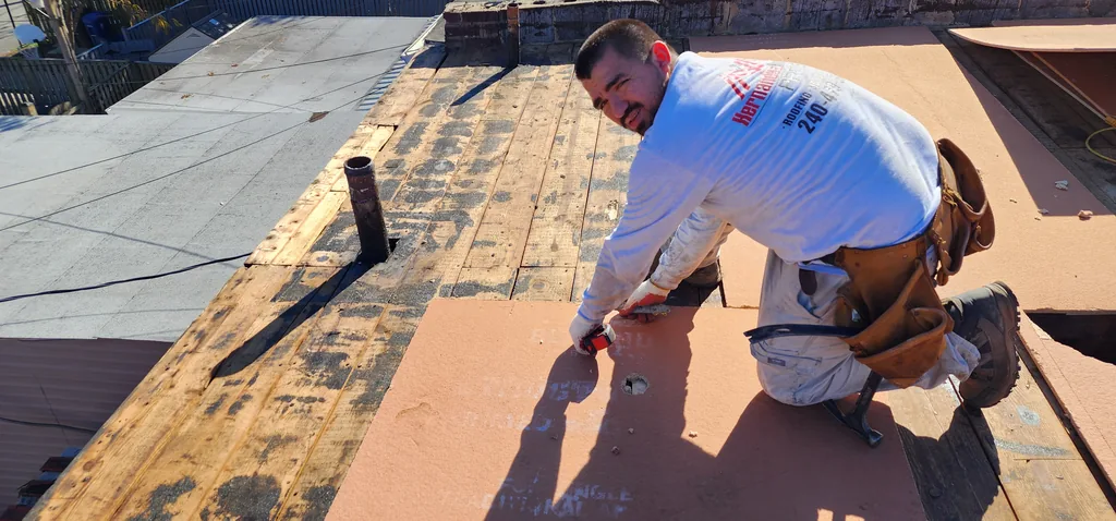 Hernandez Roofing Pros crew member in a branded company shirt working on a roof surface