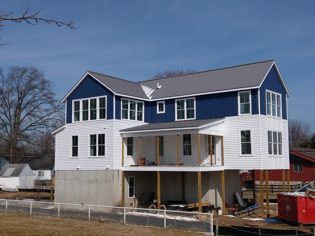 Two-storey home with a dark standing-seam metal roof and new siding during exterior work