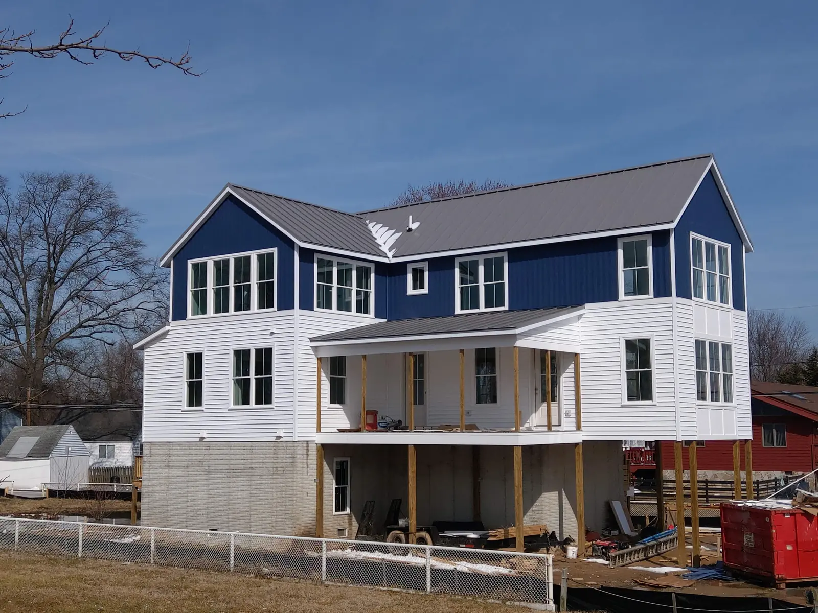Two-storey home with a dark standing-seam metal roof and new siding during exterior work