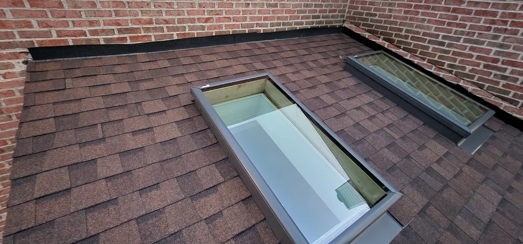 Newly installed skylights set into a completed shingle roof beside a brick wall