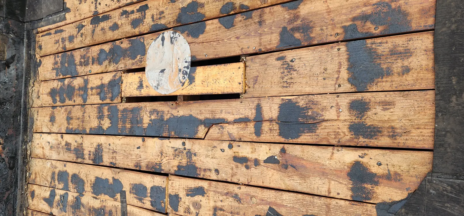 Original roof stripped back to bare wood decking, showing deteriorated boards before new material goes down