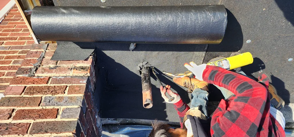 Roofer positioning torch-down membrane against a brick parapet wall during installation