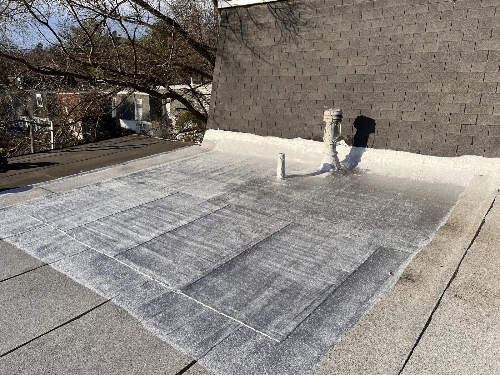 White-coated flat roof with a vent stack, finished across the full roof plane